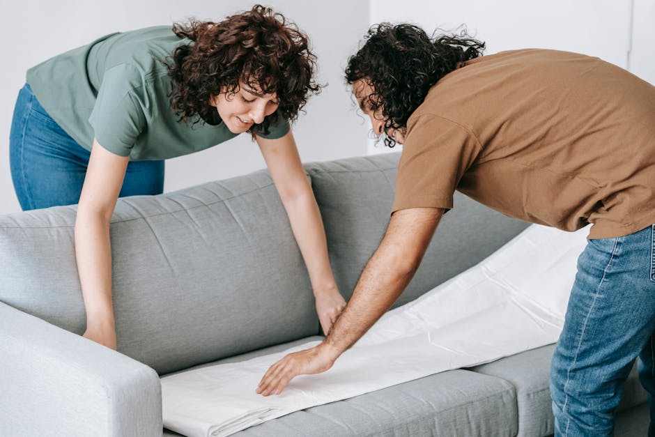 Couple covering sofa with protective cloth, preparing for moving in a modern apartment.